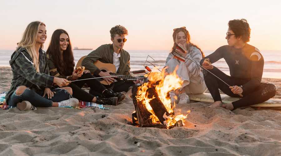 friends sitting around campfire on beach friends sitting around campfire on beach