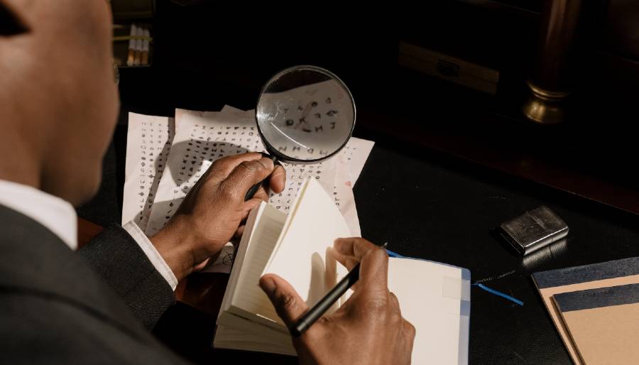 Detective uses a magnifying glass to examine a page written in code. detective with magnifying glass