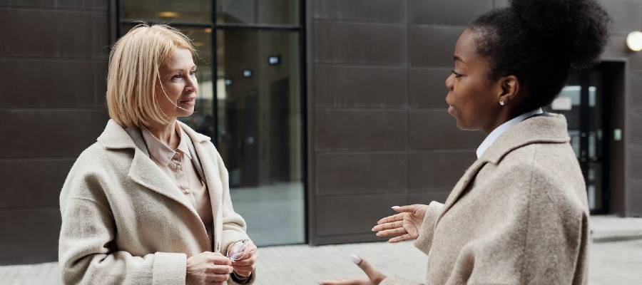 two women speaking in front of office building two women speaking in front of office building